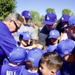 Coach giving a pep talk to a youth baseball team in blue uniforms.