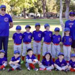 Children's baseball team posing with coaches in blue uniforms on a sunny field.