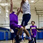 Two young basketball players jump to reach the ball during a game.