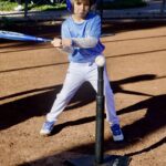 Young boy hitting a baseball off a tee on a sunny day.