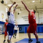 Two basketball players jumping to shoot and block the ball indoors.