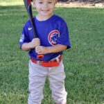 Young boy in Cubs baseball uniform holding a bat on grass.