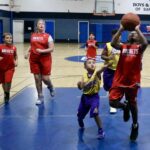 Girls playing basketball indoors, one attempting a shot.