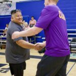 Two men shake hands warmly in a gymnasium.