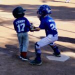 Two young baseball players at home plate, one batting and one catching.