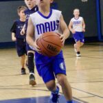 Boy in blue Mavs jersey dribbling basketball on court.