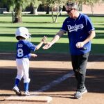 A coach gives a high-five to a young baseball player at home plate.