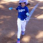 Young girl in Dodgers uniform running on a baseball field.