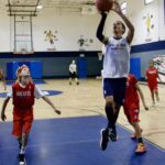 Boy in white jersey attempts a basketball shot while two defenders watch.