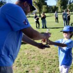 A man awards a young boy a trophy outdoors during a sunny day.