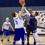 Two boys playing basketball, one shooting and one trying to block.