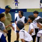 Coach giving instructions to young baseball players in a gym.