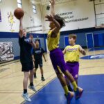 Two kids playing basketball indoors with one attempting a shot.