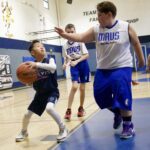 A young boy playing basketball, defended by two older players in a gym.