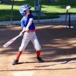 Young baseball player preparing to hit a pitch in a sunny field.
