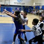 Kids play intense basketball game on indoor court.