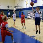 Children playing basketball indoors in a gym.
