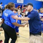 Coach shaking hands with a player in a gym filled with spectators.