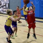 Young basketball players compete in a gym, with one shooting the ball.