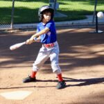 Young baseball player preparing to swing at pitch during a sunny game.