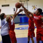 High school basketball players contesting a rebound in a gym.
