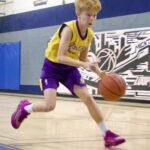 Young boy dribbling a basketball on an indoor court.