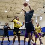Basketball player jumps to shoot while defenders try to block.
