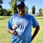 Man smiling outdoors holding a trophy, wearing a Royals t-shirt and cap.