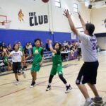 Kids playing basketball in a gym with a coach defending.