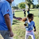A child playing baseball with an adult coach in a park.