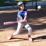 Young child hitting a baseball with a pink bat on a sunny day.