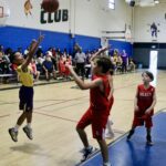 Young basketball player takes a jump shot while defenders watch.