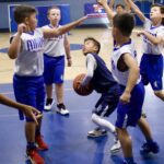 Kids playing basketball in a gym, focusing on a player with the ball.