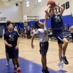 A young basketball player jumps to shoot while others watch in a gym.