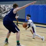 Young basketball player dribbling past a defender in a gym.