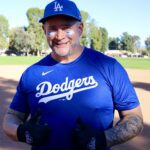 Smiling man in Dodgers baseball attire giving thumbs up on field.