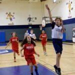 Children playing basketball indoors, one boy jumping to shoot.